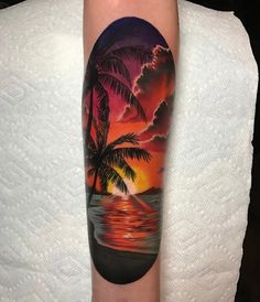 a person with a sunset and palm tree tattoo on their arm, next to a white towel