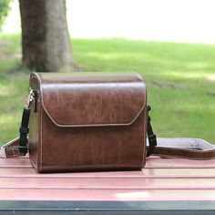 a brown leather bag sitting on top of a wooden table next to a green tree