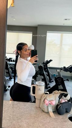 a woman taking a selfie in front of a mirror with her cell phone and gym equipment