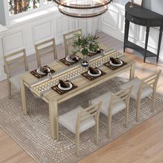 a dining room table with chairs and plates on it in front of a chandelier