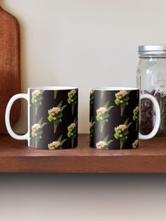 two coffee mugs sitting on top of a wooden shelf next to a glass jar