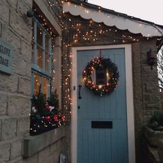 a blue front door with christmas lights and wreath on the side of an old brick building