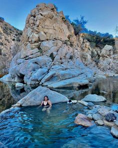 a woman sitting in the middle of a pool surrounded by rocks