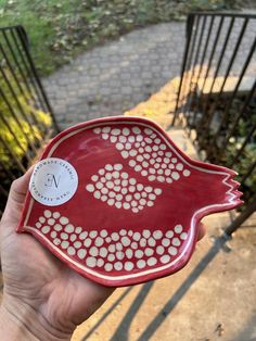 a hand holding a red bird shaped dish with white dots on it's side