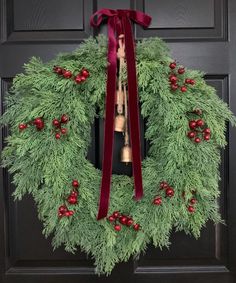 a green wreath with red berries and bells hanging on a black front door decorated for christmas