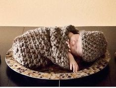 a baby is sleeping in a crocheted hat on top of a wooden table