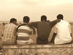 four men sitting on a wall looking out at the water and sand in front of them