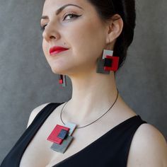 a woman in black dress wearing red and grey earrings with square shapes on it's sides