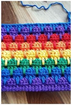 a multicolored crocheted purse sitting on top of a wooden floor next to a string