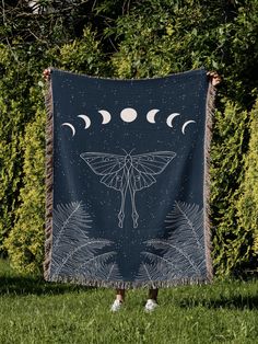 a woman holding up a blanket with the moon and moth on it in front of some bushes