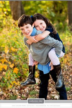 two young children hugging each other in the woods with leaves on the ground behind them