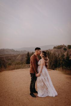 a bride and groom kissing in the middle of a dirt road with mountains in the background