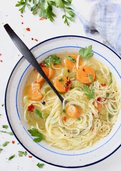 a bowl of soup with noodles, carrots and parsley