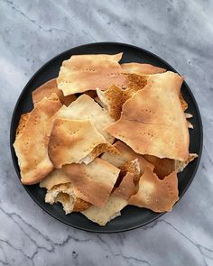 a black plate topped with tortilla shells on top of a marble counter