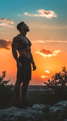 a man standing on top of a rock with the sun setting in the back ground