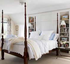 a bed with white linens and pillows in a bedroom next to bookshelves