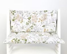 a white bench with flowers on it against a wall