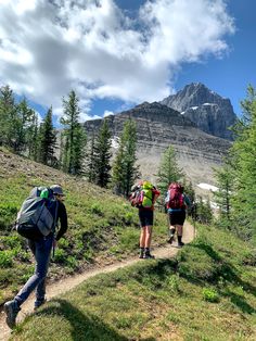 three people hiking up a hill with mountains in the background