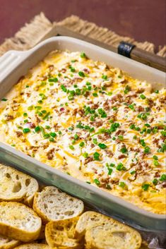 a casserole dish with cheese and green onions in it next to sliced bread