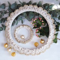 a white crochet wreath with gold ornaments and greenery on the table next to it