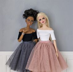 two dolls standing next to each other in front of a gray and white wall,