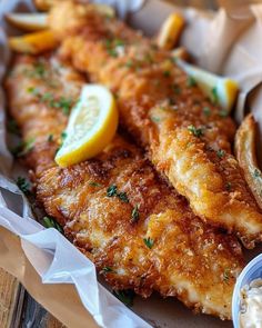 fried fish and fries with lemon wedges on the side are served in paper wrappers