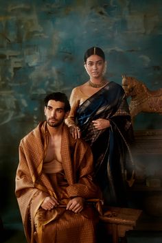 a man and woman sitting next to each other in front of a blue wall with an animal statue behind them