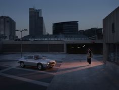 a person standing in the middle of a parking lot next to a parked car at night