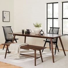 a wooden table with two black chairs and a white rug on the floor next to it