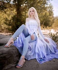 a woman sitting on top of a rock in a blue and white dress with long sleeves