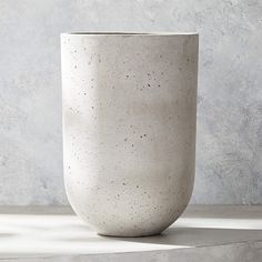 a white vase sitting on top of a table next to a gray wall and floor