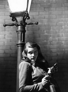 an old black and white photo of a woman sitting next to a lamp post holding a cell phone