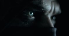 a man's face with green eyes in the dark