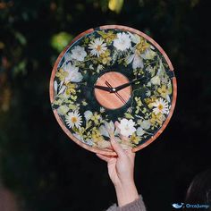 a person holding up a clock with flowers on it