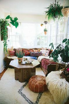 a living room filled with lots of furniture next to a white wall and window covered in plants