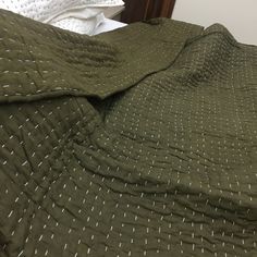 an unmade bed with green bedspread and white dots