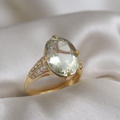 an oval shaped green amethorate and diamond ring sitting on a white cloth