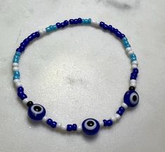 Beaded evil eye bracelet. Blue and white. Adjustable Blue Evil Eye Bracelet Hand-strung, Adjustable Blue Hand-strung Evil Eye Bracelet, Handmade Blue Stretch Bracelet For Festivals, Blue Spacer Beads Bracelets For Festivals, White Evil Eye Beaded Bracelets, Turquoise Bracelets With Evil Eye Round Beads, Blue Festival Bracelets With Spacer Beads, White Beaded Round Evil Eye Bracelet, Blue Evil Eye Bracelet With Round Beads