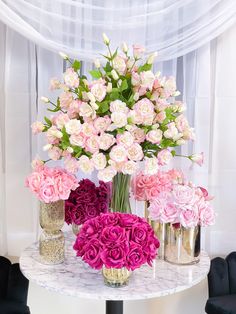 a table topped with vases filled with pink and white flowers next to black chairs