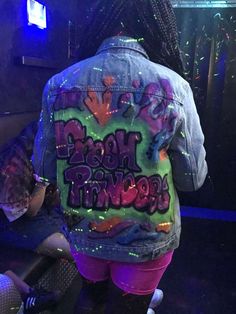 a woman wearing a jean jacket with neon paint on it