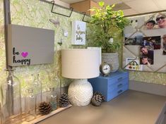 a desk with a lamp, vases and pictures on the wall behind it that says be happy