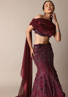 Featuring our whimsical wine jeweled lehenga paired with a stylized blouse that is a beautiful amalgamation of opulence and charm. Accented with sparkly jewels this fish cut silhouette wraps your curves with elegance and grace. The stylized blouse elevated with feminine trail draping and wide neck fit complete this grandeur effortless look. Dry clean only if required. Slight variation in color is possible due to digital photography. Modern Indian Wedding Guest Outfit, Embellished Wedding Sets, Elegant Purple Choli With Traditional Drape, Elegant Hand Embellished Purple Sets, Glamorous Embellished Lehenga With Traditional Drape, Elegant Red Lehenga With Sequins, Glamorous Hand Embellished Lehenga, Elegant Purple Choli For Wedding, Elegant Embellished Purple Choli