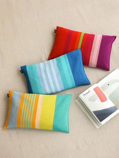 three colorful striped pillows sitting on top of a bed next to an open book and magazine