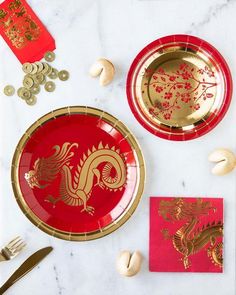 red and gold plates with golden dragon designs are on a white marble tablecloth next to silverware