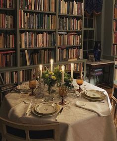 the table is set with plates and place settings in front of a bookcase full of books