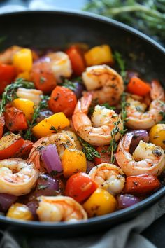 Shrimp sautéed with colorful bell peppers, cherry tomatoes, and red onions in a skillet, garnished with herbs.