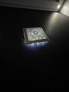 a square light fixture sitting on top of a black floor next to a window in a building