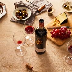 a table topped with wine glasses filled with red wine next to cheese and olives