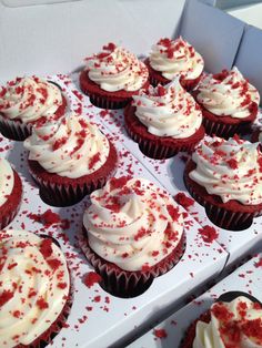 cupcakes with white frosting and red sprinkles in a box