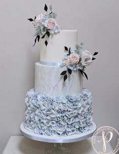 a three tiered white and blue cake with flowers on top